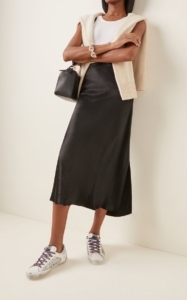 woman leaning against wall with black skirt and sneakers on
