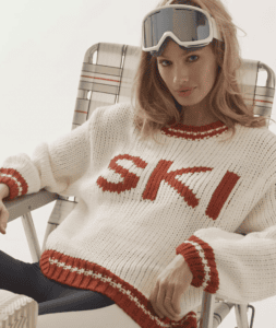 Woman sitting in chair wearing a white and red Ski sweater and ski goggles