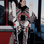 Woman wearing bold ski outfit holding skis outside a gondola