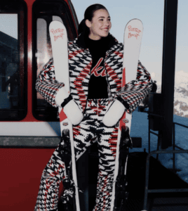 Woman wearing bold ski outfit holding skis outside a gondola