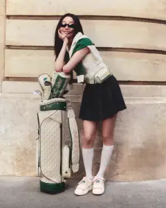 brunette woman standing next to luxury golf clothes wearing Jimmy Choo